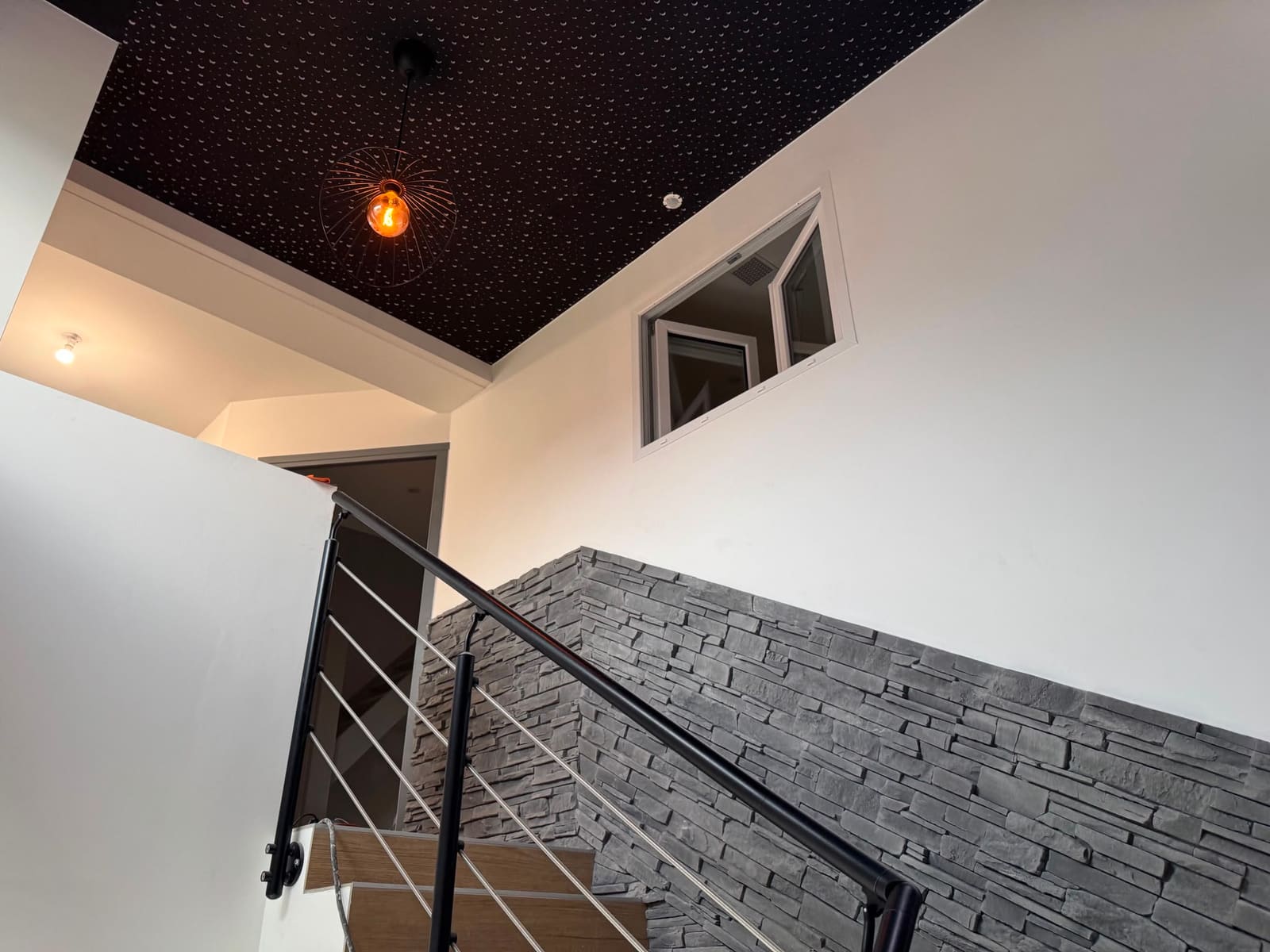 Cage d'escalier rénovée avec plafond noir étoilé, spots encastrés et mur en pierre de parement